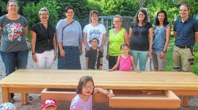Kinder und Eltern hinter einem langen Holztisch aus Douglasie im Garten des Kindergartens